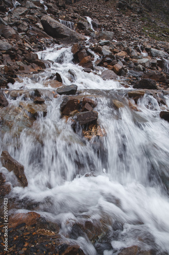 Waterfall in a high gorge among the brown rocks and fog of the Altai mountains.