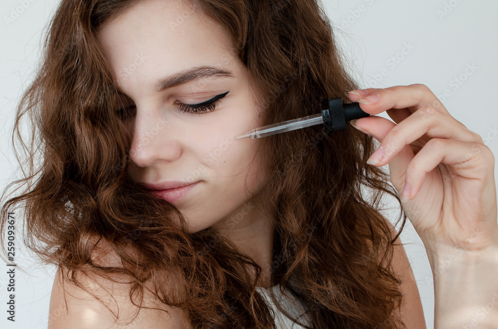Obraz premium young beautiful curly woman uses white serum for face. The concept of facial skin and hair care.