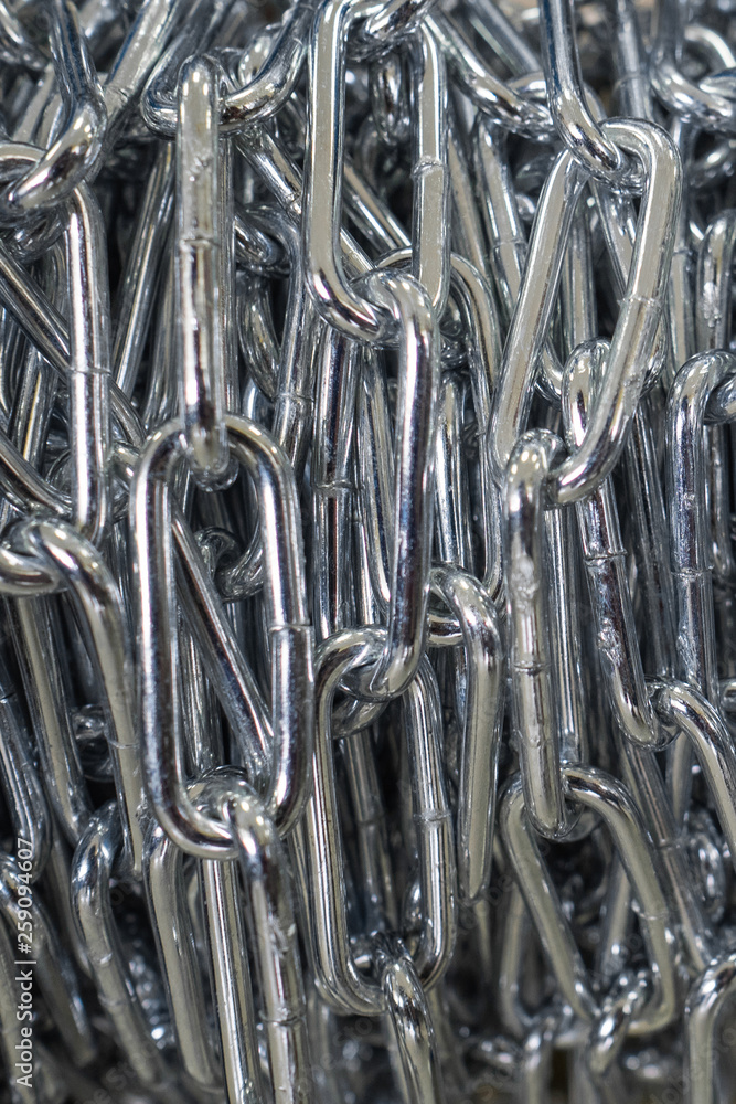 The steel chain is reeled up on the coil in shop. The brilliant chain twisted in a roll. Long industrial chain The steel chain is reeled up on the coil in shop. The brilliant chain twisted in a roll. Long industrial chain