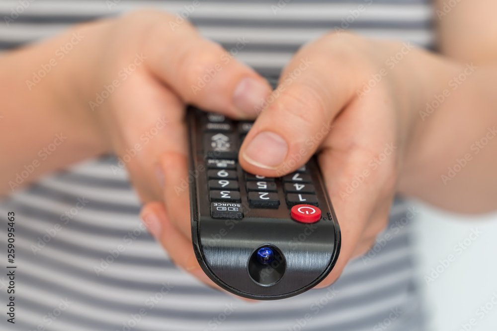 Remote control in female hands pointing to TV