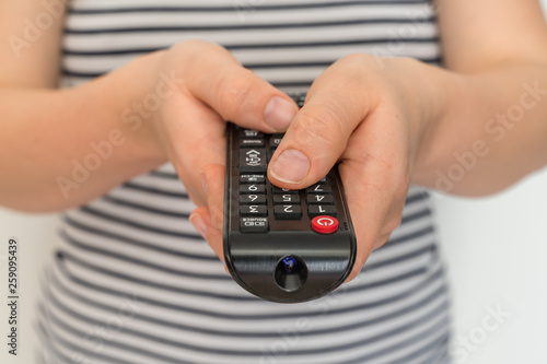 Remote control in female hands pointing to TV