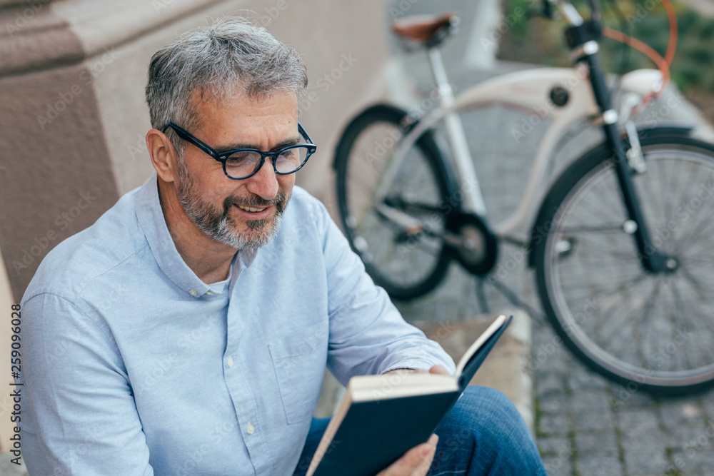 leisure time in town. man reading book , blurred bicycle in background leisure time in town. man reading book , blurred bicycle in background