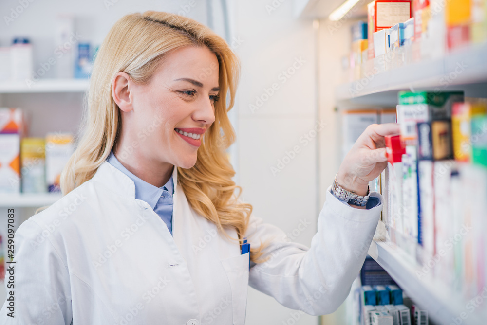 Smiling pharmacist taking medicine from a shelf, close-up.