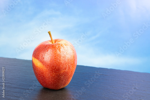 Fresh red apple fruit with water drops, blue sky background and copy space