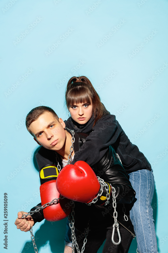 Bad games. Close up fashion portrait of two young cool hipster girl and boy wearing jeans wear. Studio shot of two serious best friends having fun over blue background. Bad games. Close up fashion portrait of two young cool hipster girl and boy wearing jeans wear. Studio shot of two serious best friends having fun over blue background.