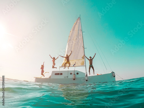 Happy crazy friends diving from sailing boat into the sea - Young people jumping inside ocean in summer vacation - Main focus on left girls - Travel and fun concept - Fisheye lens distortion © DisobeyArt