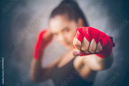 Image focus the fist of the beautiful young Asian boxers. She is a martial arts athlete, strong face filled with sweat, Two of her hands with red boxing bandage hand wrap. Woman power with copy space.