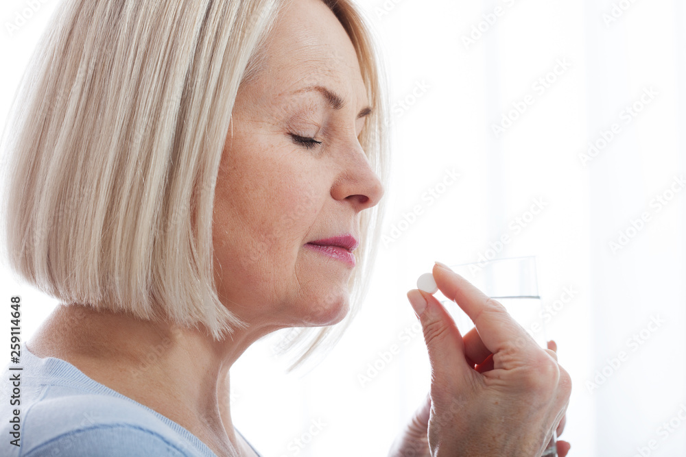Doubtful sick ill middle woman holding pill and glass of water taking painkiller medicine drugs to relieve headache pain, worried about side effects of antidepressant or emergency contraceptive meds Doubtful sick ill middle woman holding pill and glass of water taking painkiller medicine drugs to relieve headache pain, worried about side effects of antidepressant or emergency contraceptive meds