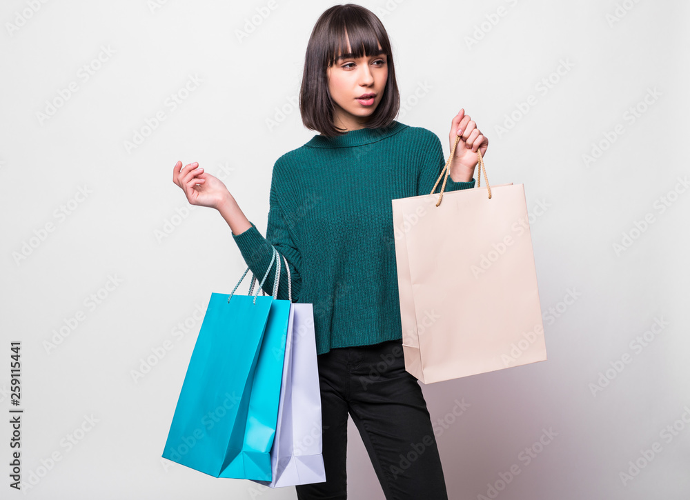 Fototapeta premium Portrait of a smiling woman dressed in green sweater holding shopping bags and looking away isolated over white background
