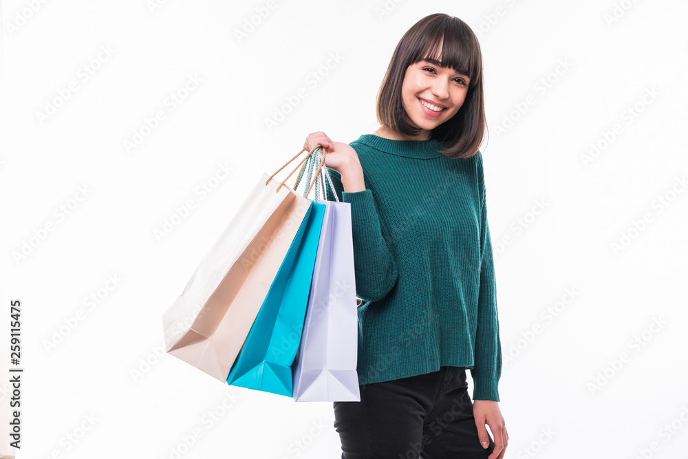 Full-length shot of a young girl with green sweater holding a lot of shopping bags on isolated white background