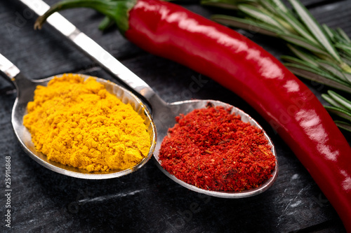 Turmeric and red hot pepper on spoon on dark wooden background. Spices of Indian cuisine, close-up