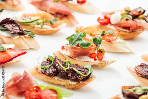 selective focus of italian bruschetta with dried tomatoes, prosciutto and herbs on white