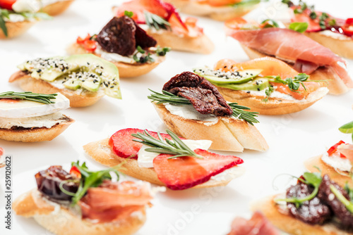 selective focus of italian bruschetta with dried tomatoes, prosciutto, avocado, strawberries and herbs