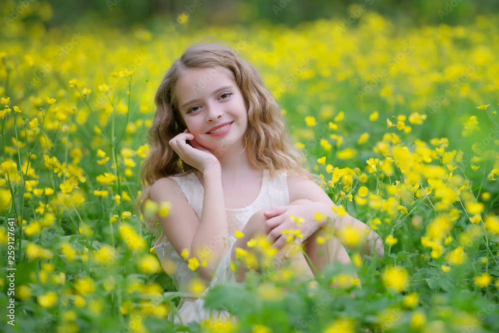 A cute young girl is in the forest on the edge of the forest with yellow flowers. She has blond curly hair, she's wearing a beautiful dress. A cute young girl is in the forest on the edge of the forest with yellow flowers. She has blond curly hair, she's wearing a beautiful dress.