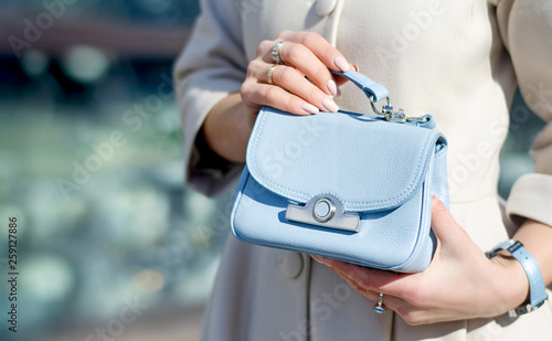 Blue little handbag in female hands. Close-up leather handbag. Women walking in the city. Girl in a beige coat.