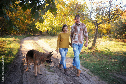 Smiling young adult love couple walking in park with their german shepherd dog, holding hands , young family portrait © LP Design