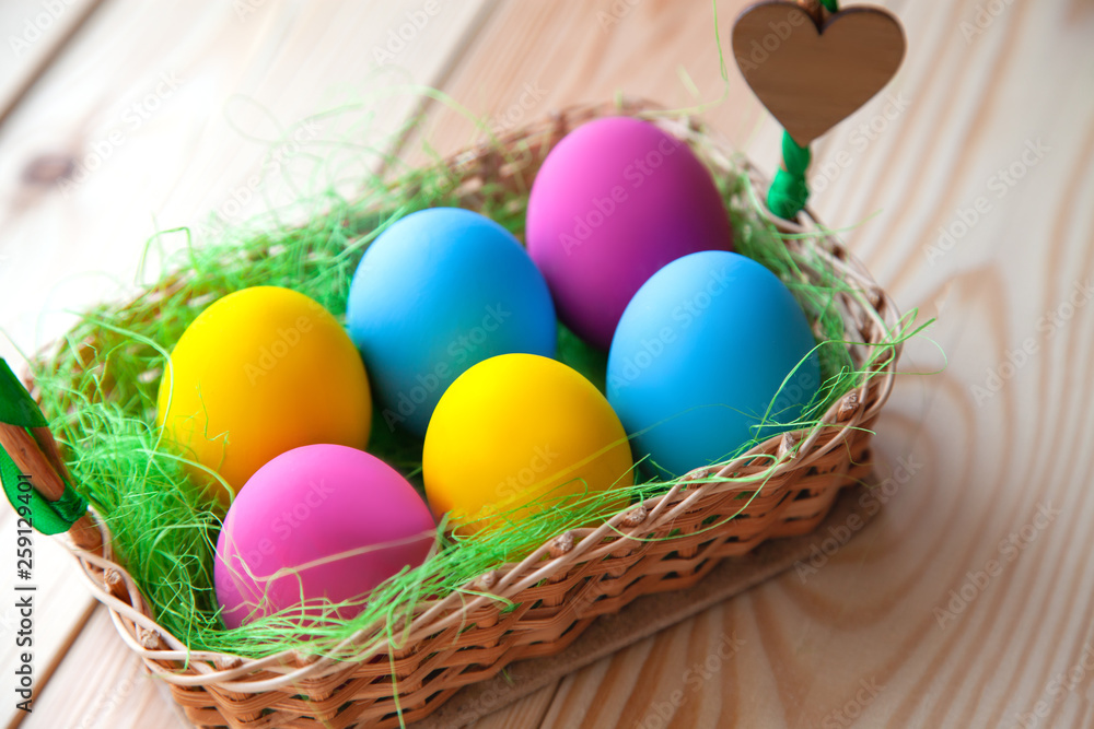 colored easter eggs in wicker basket, on wooden background