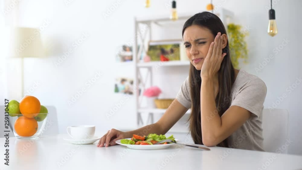 Woman eating salad, feeling tooth ache from excess acid in products, health Woman eating salad, feeling tooth ache from excess acid in products, health