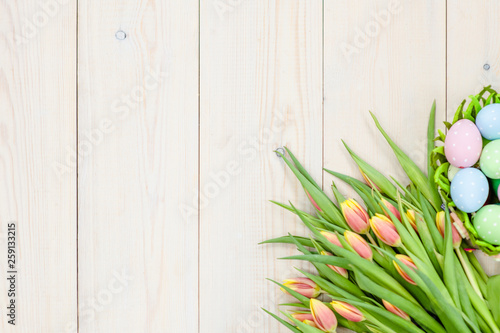 Tulips  with easter eggs in basket over wooden background.  Backdrop with empty space for text. Top view. Floral mockup concept