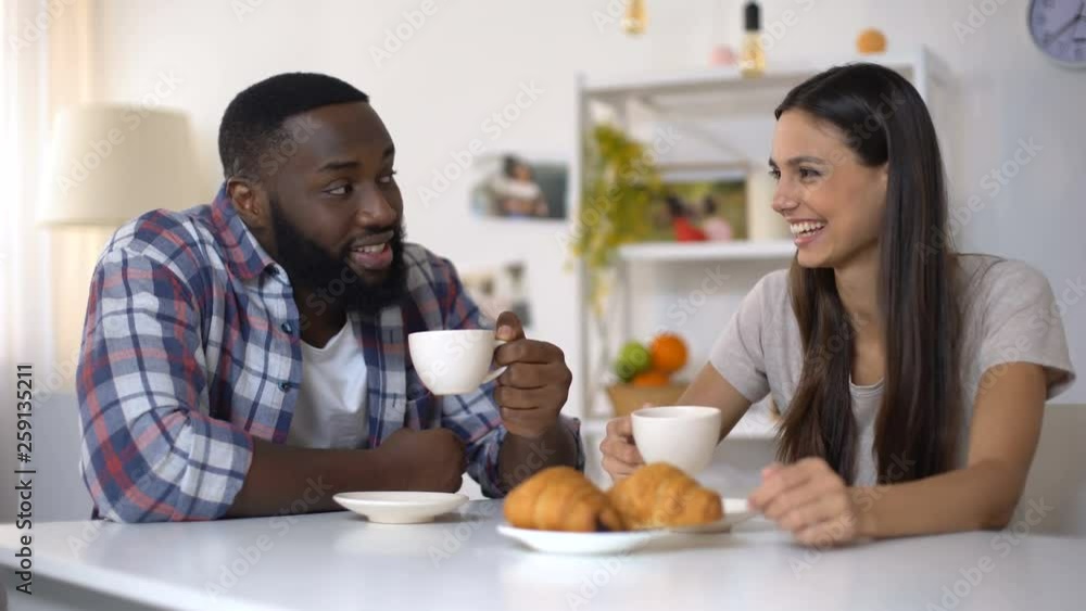 Mixed-race couple talking and laughing during breakfast at home, morning coffee Mixed-race couple talking and laughing during breakfast at home, morning coffee