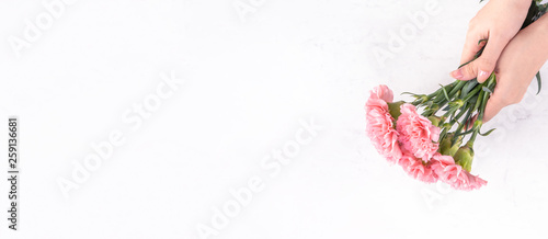 Fototapeta Naklejka Na Ścianę i Meble -  Woman giving bunch of elegance blooming baby pink color tender carnations isolated on bright marble background, mothers day decor design concept, top view, close up, copy space