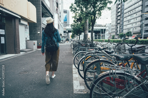 Parking for bicycles on the street rent a bike and walking around city in osaka japan. back view full length young asian woman in hat sightseeing busy urban residential area. female relax sunny day