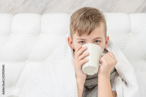 Papier peint Cozy ill boy with flu sitting in bed and drinking tea at home
