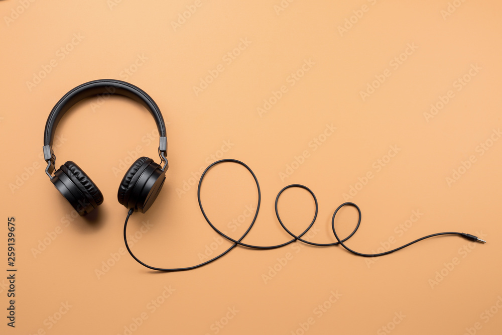 Photo of stylish modern black headphones over beige background. Photo of stylish modern black headphones over beige background.