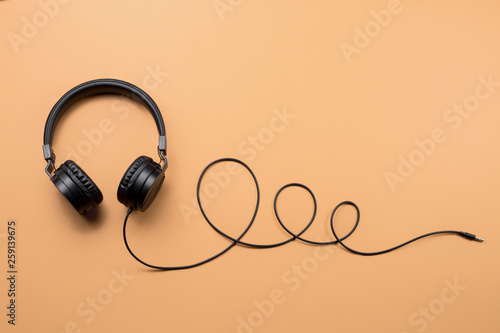 Photo of stylish modern black headphones over beige background.