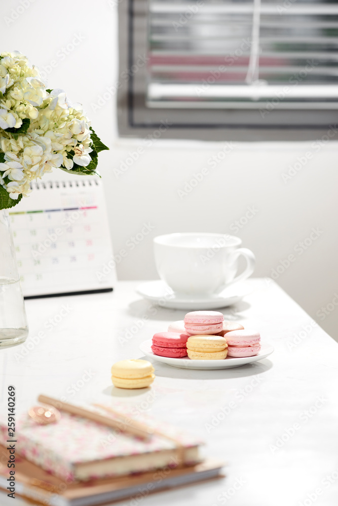 Office table desk. Feminine desk workspace frame with calendar, diary, hortensia bouquet, macaron and coffee on white background. ideas, notes or plan writing concept Office table desk. Feminine desk workspace frame with calendar, diary, hortensia bouquet, macaron and coffee on white background. ideas, notes or plan writing concept