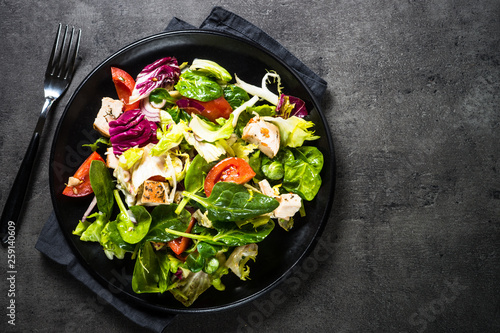 Green salad with chicken and vegetables on black.