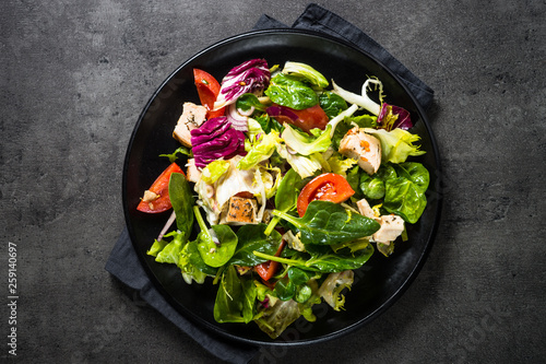 Green salad with chicken and vegetables on black.