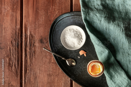 An overhead photo of a soft-boiled egg in an egg server with coarse sea salt and a spoon, on a dark rustic wooden table with copy space