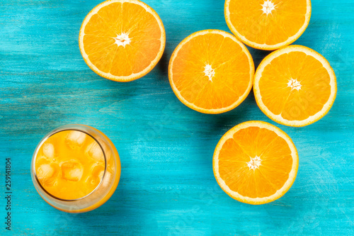 A glass of fresh orange juice with orange halves, shot from above on a vibrant blue background forming a frame with a place for text