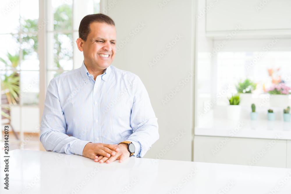 Middle age man sitting at home looking away to side with smile on face, natural expression. Laughing confident.