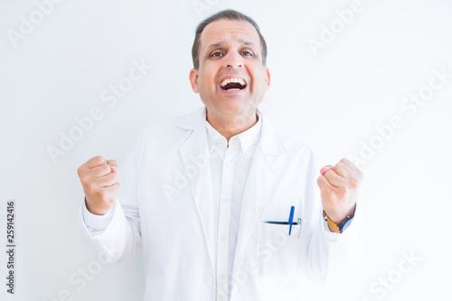 Middle age doctor man wearing medical coat over white background celebrating surprised and amazed for success with arms raised and open eyes. Winner concept.