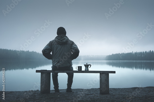 A man sits on a bench near the lake in the forest. View from the back.