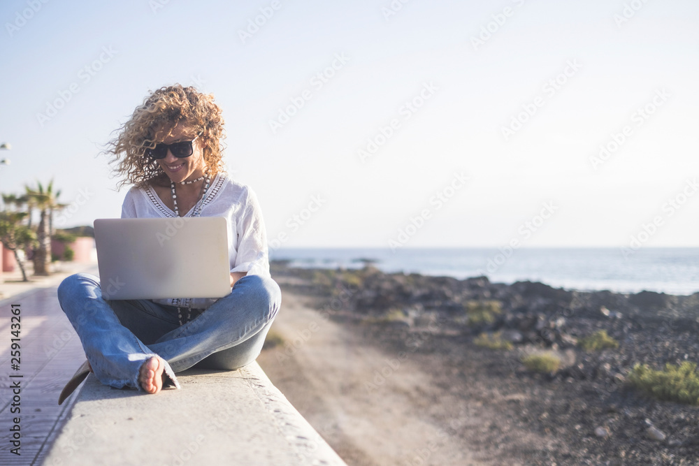 Curly attractive young caucasian woman work at the laptop in outdoor near the beach - internet everywhere and freelance digital nomad concept for free people enjoying the lifestyle