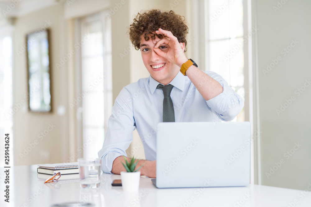 Young business man working with computer laptop at the office doing ok gesture with hand smiling, eye looking through fingers with happy face. Young business man working with computer laptop at the office doing ok gesture with hand smiling, eye looking through fingers with happy face.