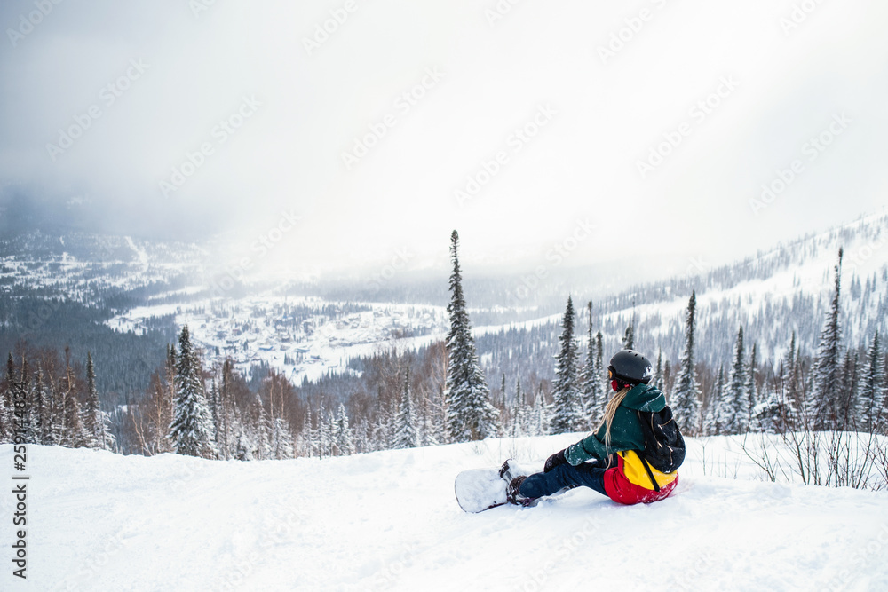 Female snowboarder freerider sitting in the mountains on a snowy slope.