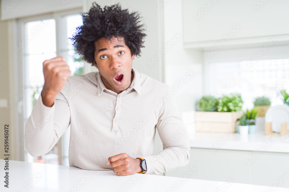 African American man at home angry and mad raising fist frustrated and furious while shouting with anger. Rage and aggressive concept. African American man at home angry and mad raising fist frustrated and furious while shouting with anger. Rage and aggressive concept.