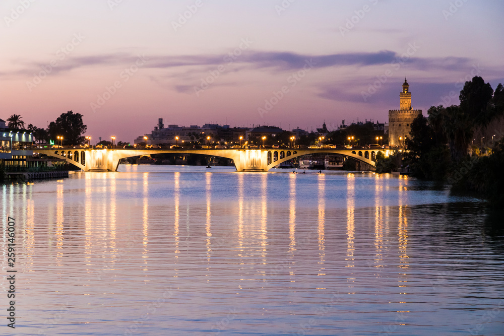 Sevilla, Spain. Views of the Guadalquivir river, with the Torre del Oro (Tower of Gold) and the Puente de San Telmo bridge at sunset