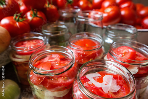 Canning fresh tomatoes with onions in jelly marinade. Woman hands putting red ripe tomato slices and onion rings in jars. Basil, parsley leaves on top of onions. Vegetable salads for winter