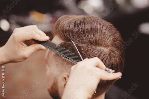 Close-up, master hairdresser does hairstyle with scissors comb. Concept Barbershop