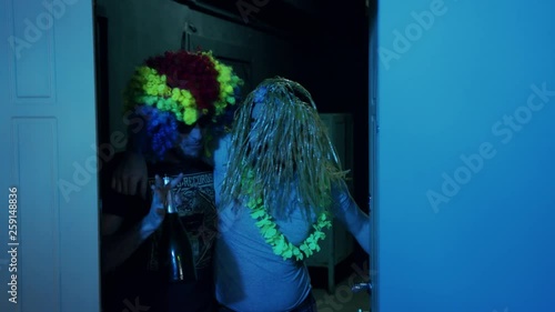 White wooden door opening and two friends coming home after costume party. Night time. Indoors. Happy drunk men wearing colored wigs. Indoors. Night time. Happiness.