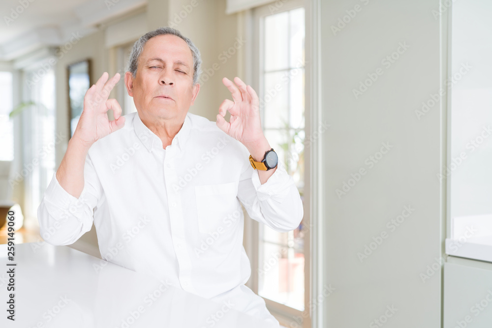 Fototapeta premium Handsome senior man at home relax and smiling with eyes closed doing meditation gesture with fingers. Yoga concept.