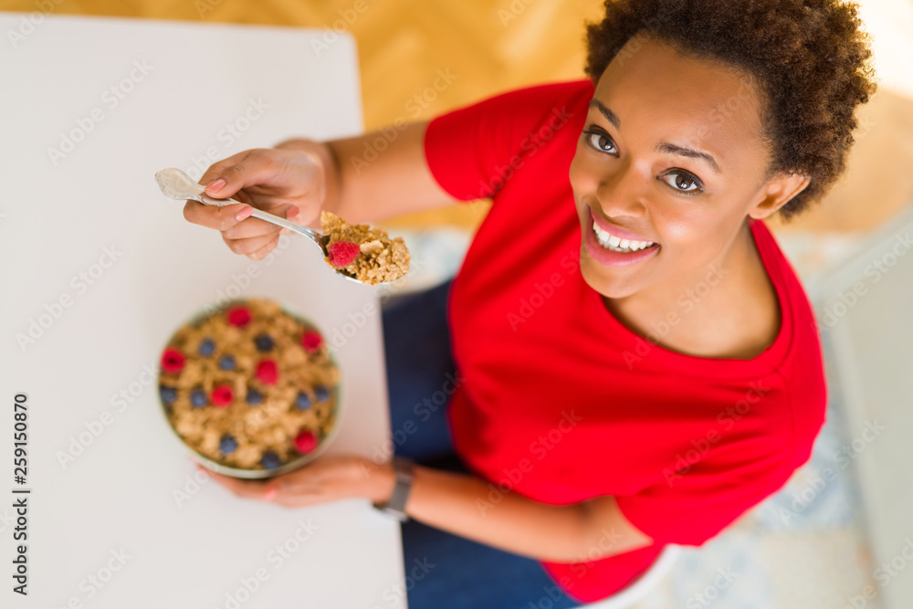 Fototapeta premium Young beautiful african american woman with afro hair eating healthy wholemeal cereals and berries as healthy breakfast