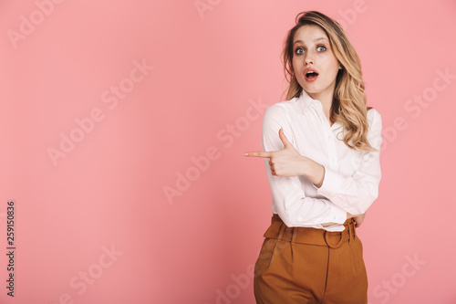 Portrait of lovely woman smiling and pointing finger at copyspace isolated over pink background