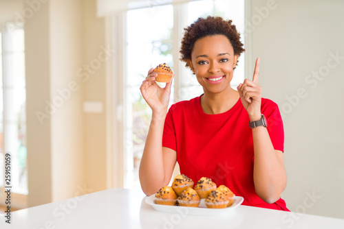 Young african american woman eating chocolate chips muffins surprised with an idea or question pointing finger with happy face, number one