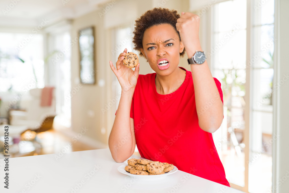 Young african american woman eating chocolate chips cookies annoyed and frustrated shouting with anger, crazy and yelling with raised hand, anger concept
